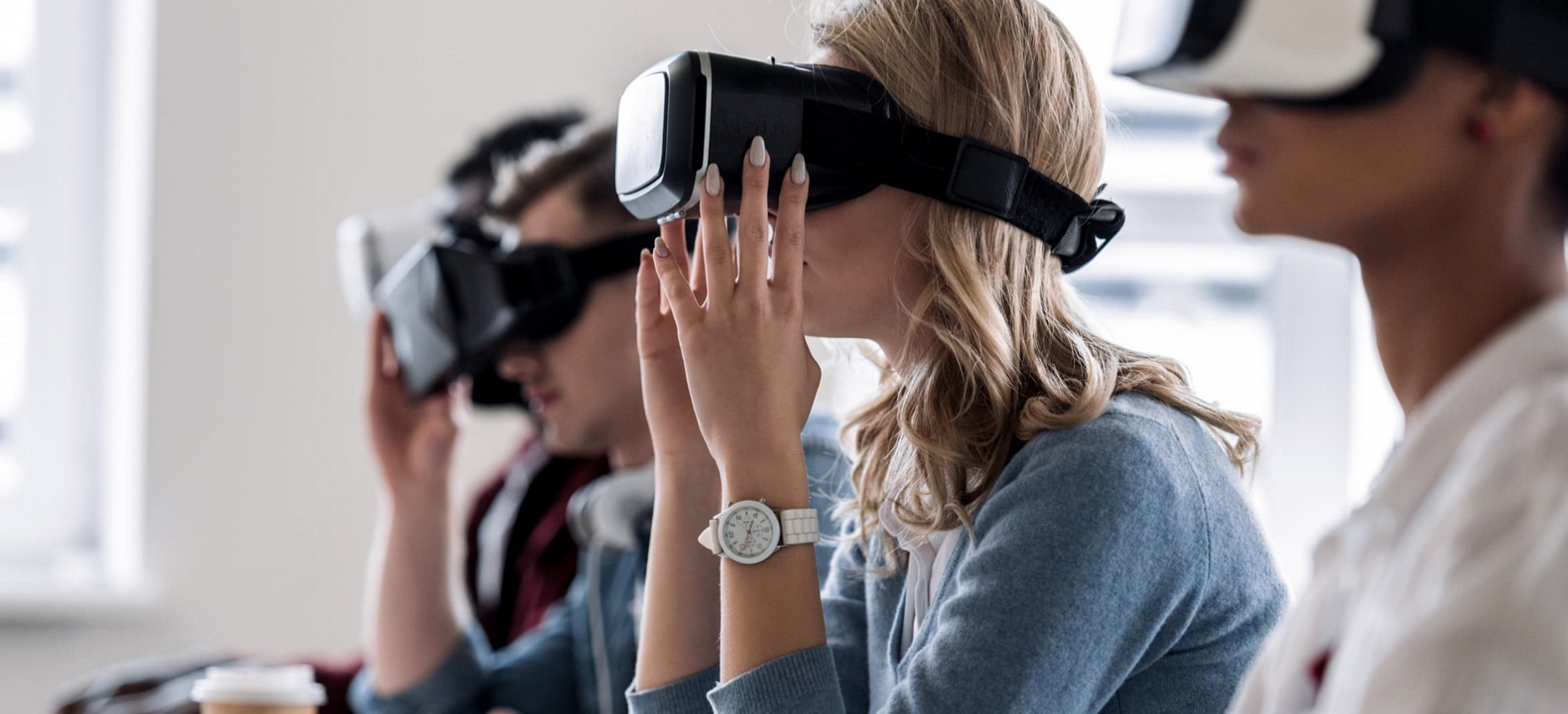 Students sit at keyboards using VR headsets to augment their learning in a classroom setting.